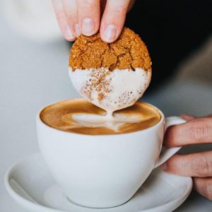 A ginger snap cookie being dunked into a latte.