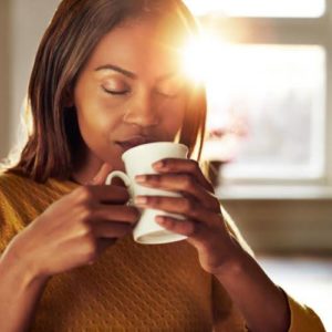 A woman smelling a fresh cup of coffee on a sunny morning day.