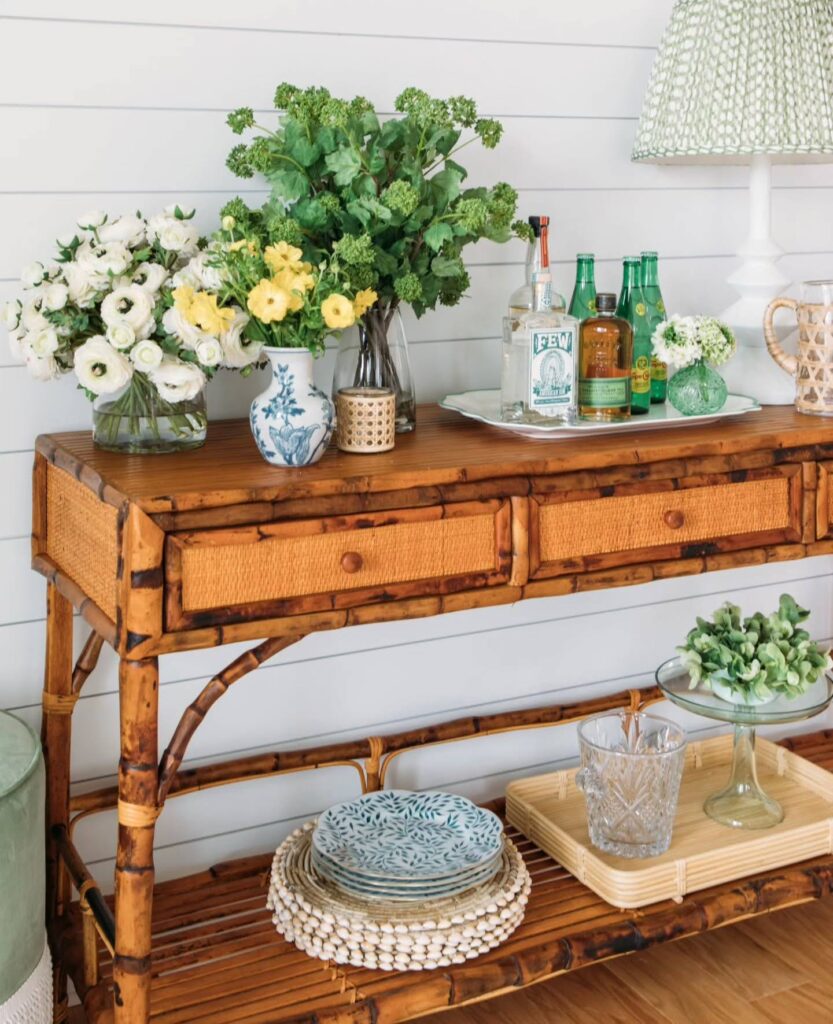 Three woven drawer table with a rattan frame with flowers and drinks in a tray sitting on top.